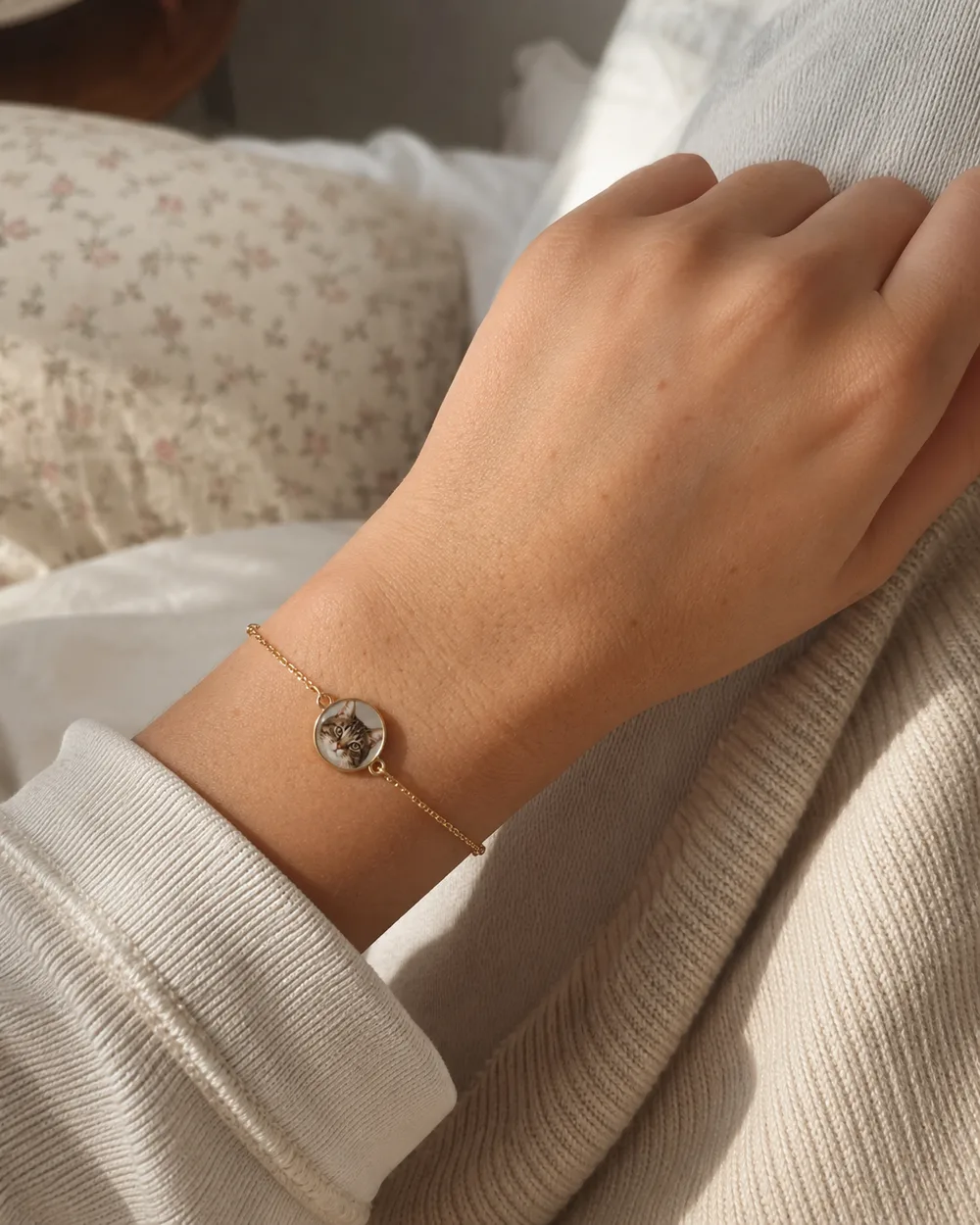 Pulsera dorada con un dije redondo que muestra el retrato de un gato atigrado, puesta en una muñeca