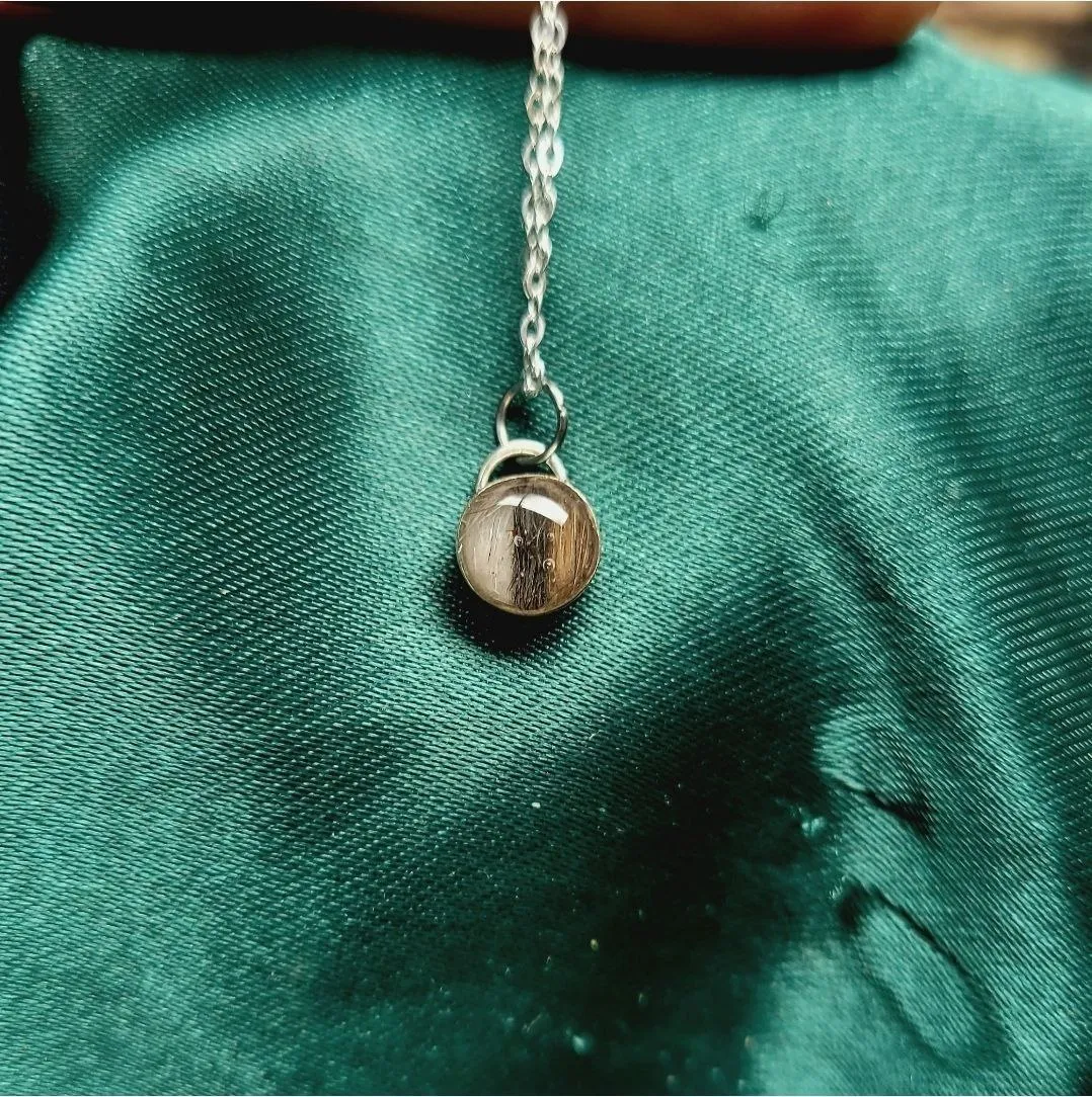 Silver necklace with a round pendant preserving a lock of pet fur, on green satin