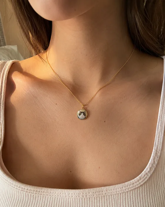 María lleva un collar dorado con un dije redondo que muestra el retrato de su gata Luna